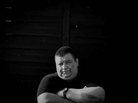 Monochrome portrait of a man with arms crossed against dark wooden background.