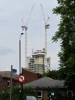 A cityscape featuring a high-rise under construction with tower cranes in the background.