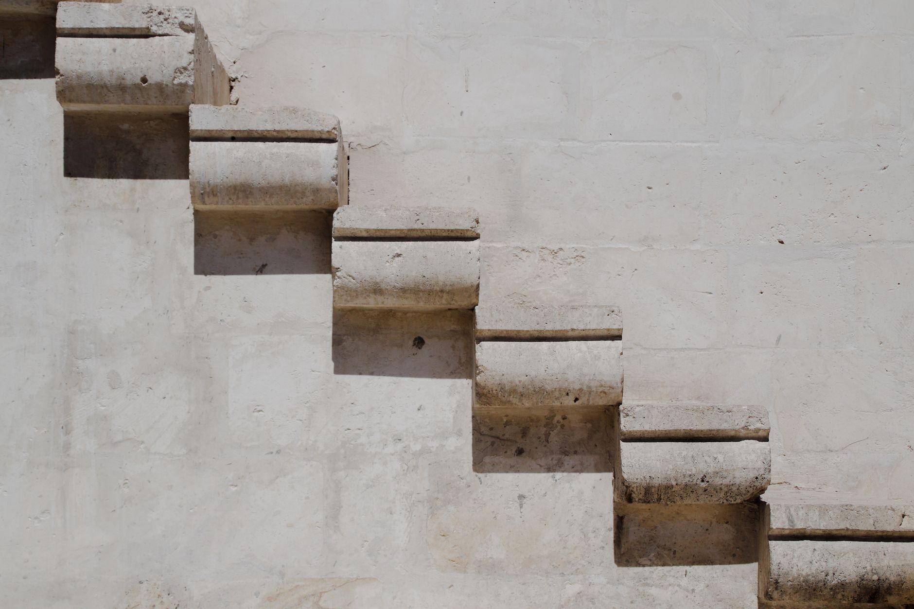 Close-up view of an ancient stone staircase against a textured white wall, offering copy space.
