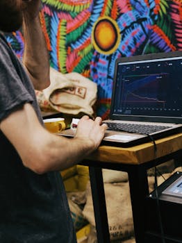 Person studies business performance graphs on a laptop in a colorful, creative cafe setting.