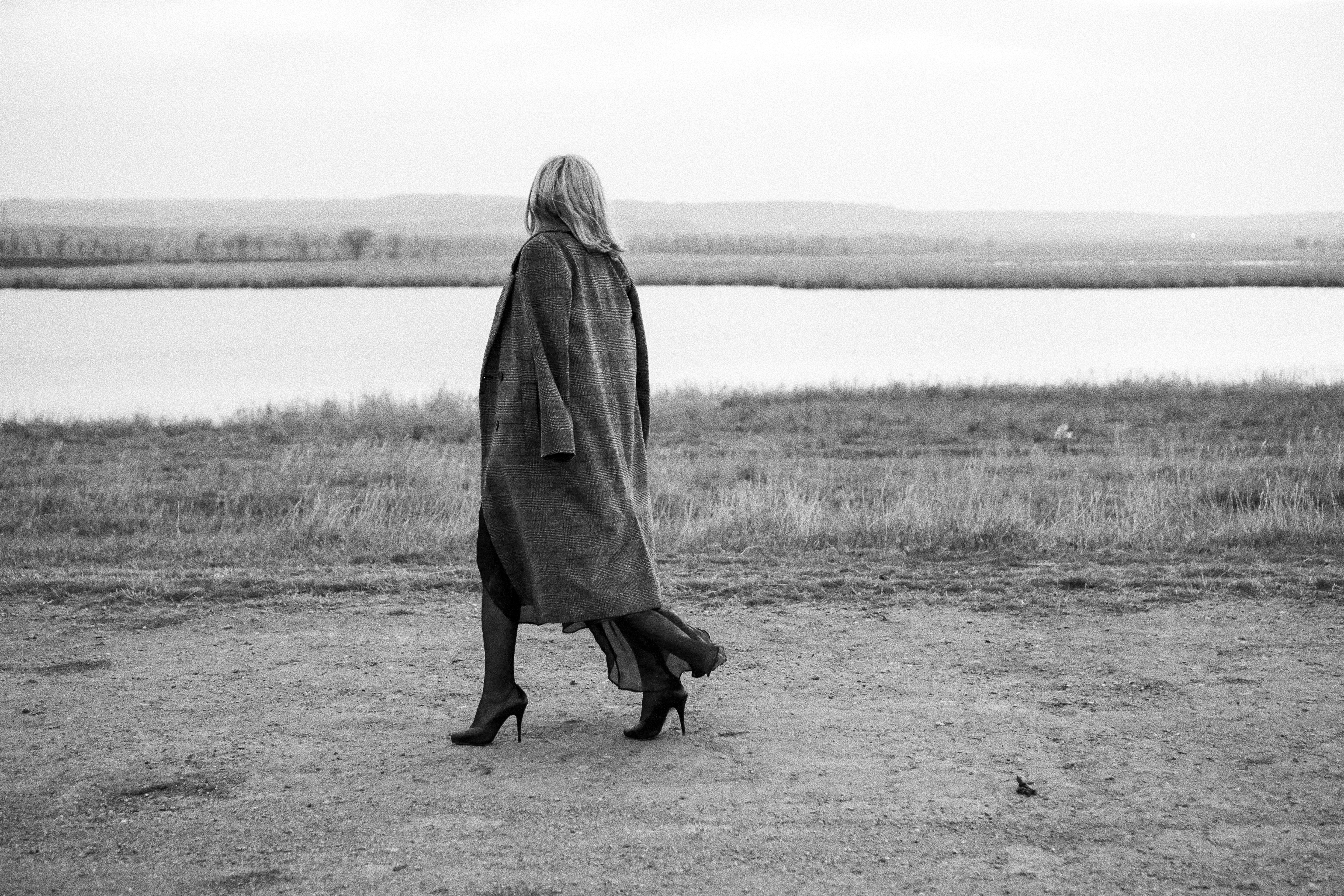 Woman Wearing Trench Coat Walking on Lakeshore · Free Stock Photo