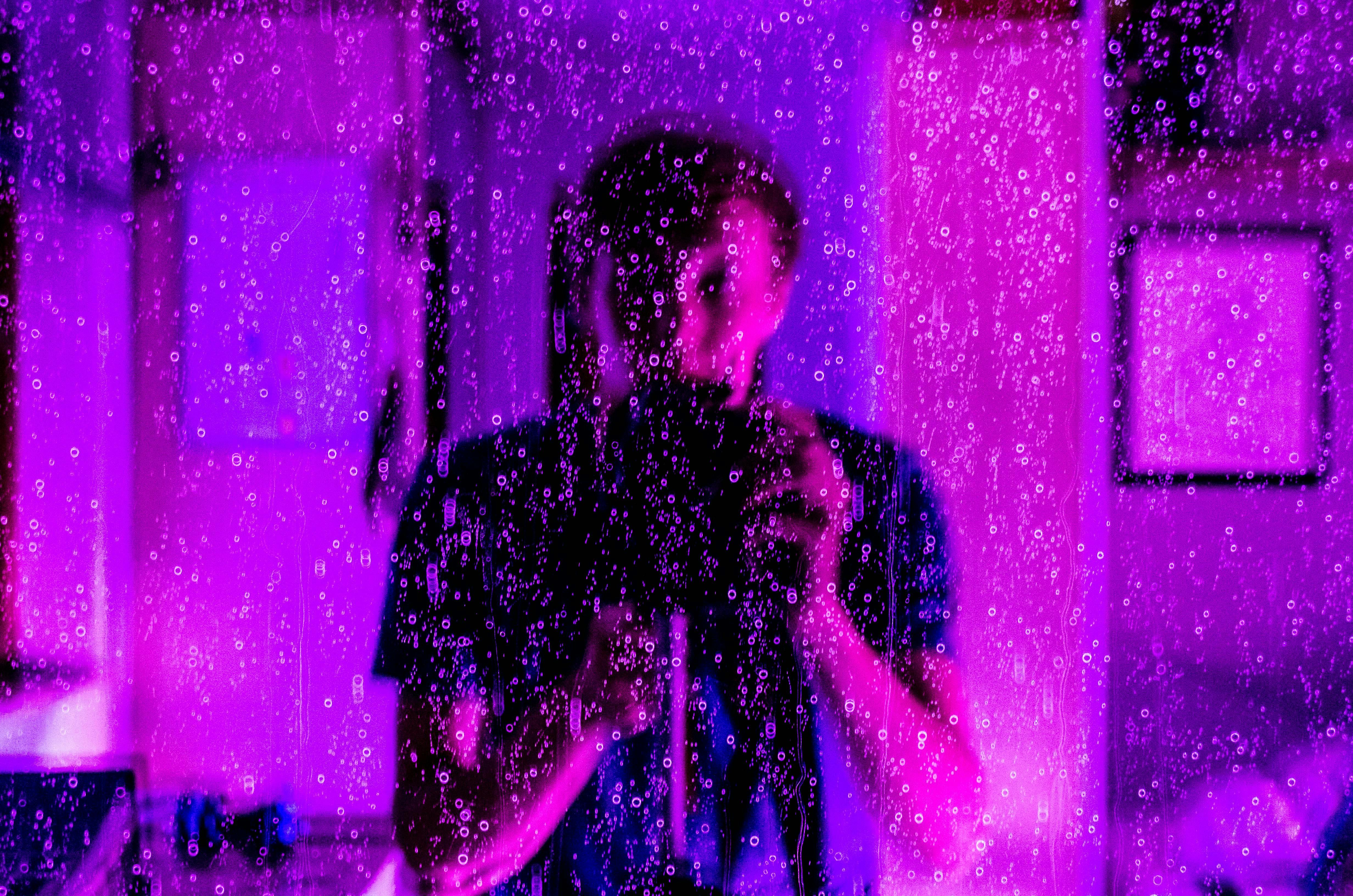 这幅富有创意的肖像画，通过雨水覆盖的玻璃和紫色灯光的倒影，展现了摄影师的视角