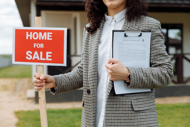 Close-up Of A Woman Holding A Home For Sale Sign