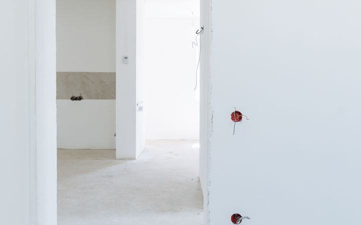 Bright unfinished room with white walls and exposed wiring, showcasing modern interior design potential.