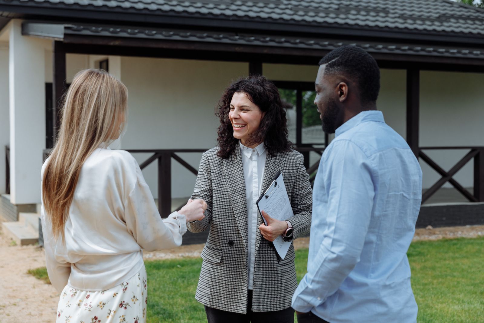 Free A real estate agent shakes hands with a couple outside a modern house, symbolizing a successful property deal. Stock Photo