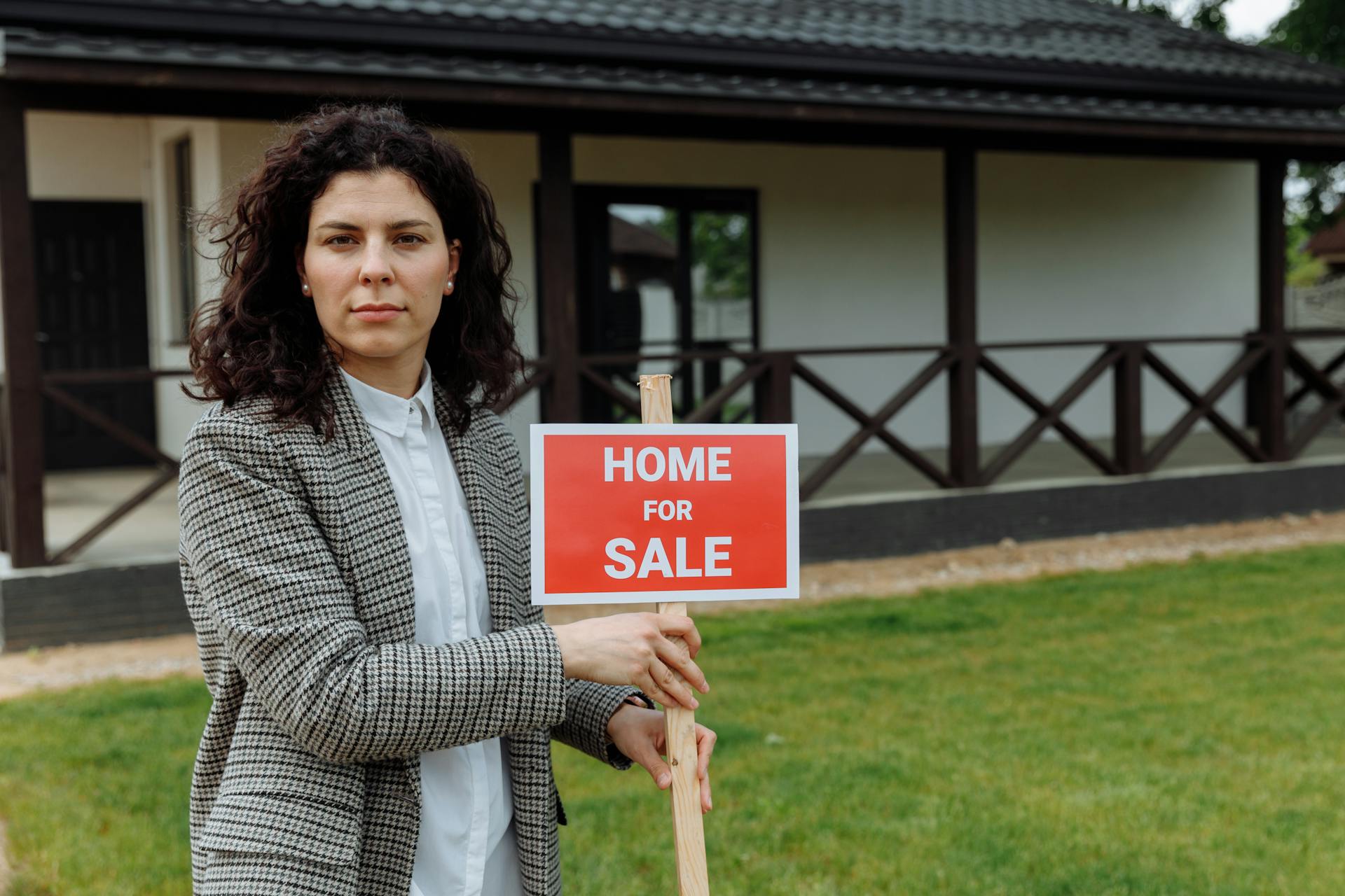 Confident real estate agent with sale sign in front of a house.