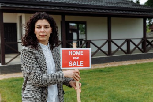 Free Confident real estate agent with sale sign in front of a house. Stock Photo