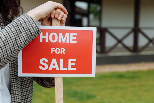 Close-up of a home for sale sign held by a person outdoors in a yard.