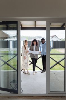 Three adults discussing real estate plans outdoors, showcasing diversity and teamwork.
