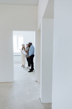 Three professionals in hard hats examining blueprints inside a residential property.