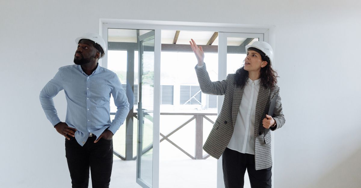 Two contractors inspecting a modern house interior wearing hard hats.