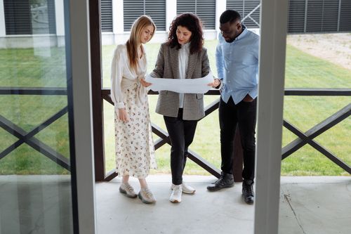 Free A realtor with clients examining a floor plan outside a modern property. Stock Photo