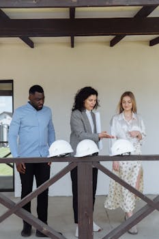 Three adults discussing on a balcony with helmets, suggesting construction or planning.