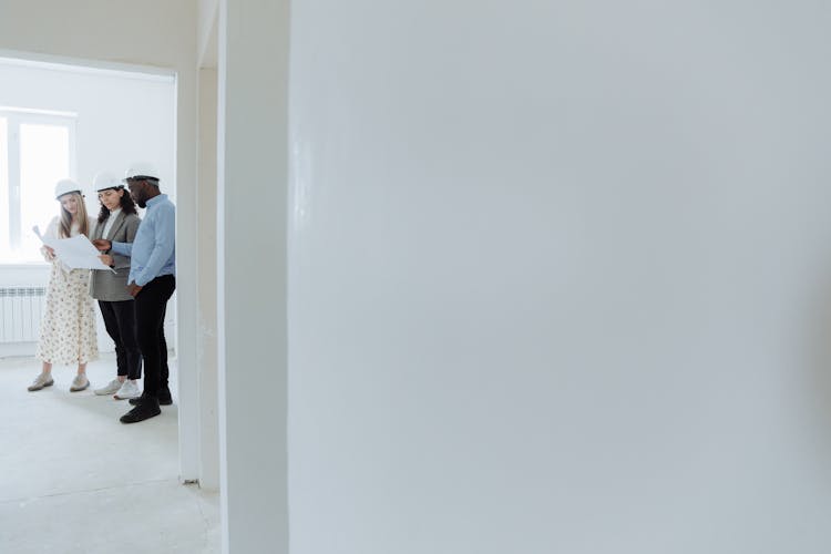 People Holding A Piece Of A Sheet Of Paper While Standing By The White Wall