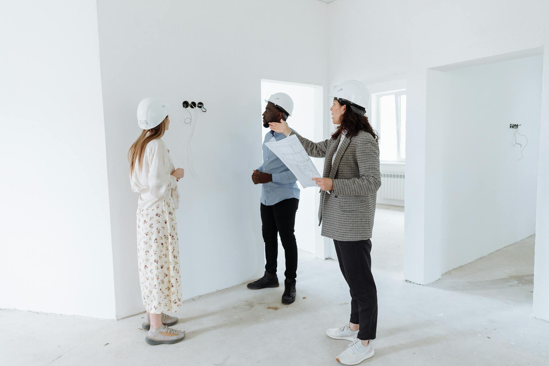 Three professionals discuss design plans inside a new house wearing hard hats.