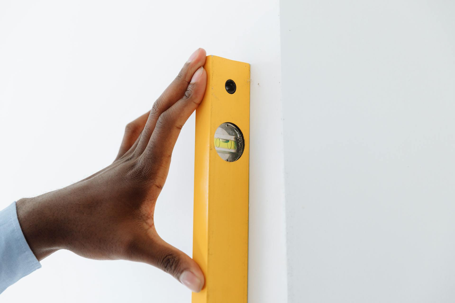 A Person Holding a Yellow Leveling Tool Against the Wall