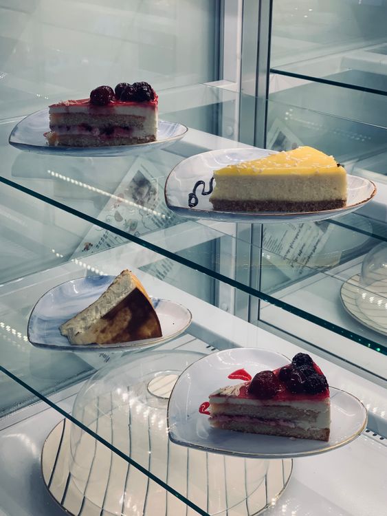 Free Four different artisan cake slices in an elegant glass display case, perfect for dessert selections. Stock Photo