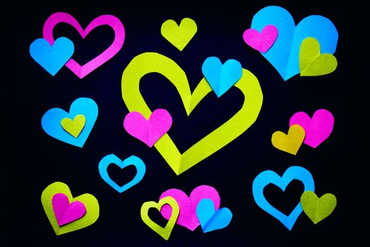 Colorful heart-shaped paper cutouts arranged creatively against a dark surface, showcasing vibrant hues.