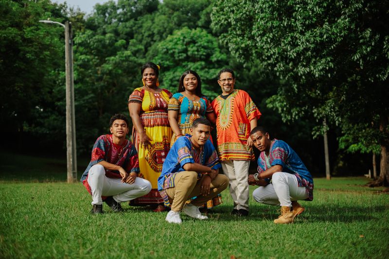 A family wearing vibrant traditional African attire posing happily in a park setting.