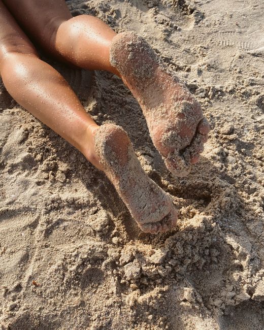 Close-up of bare feet covered in sand on a sunny beach day, capturing relaxation.