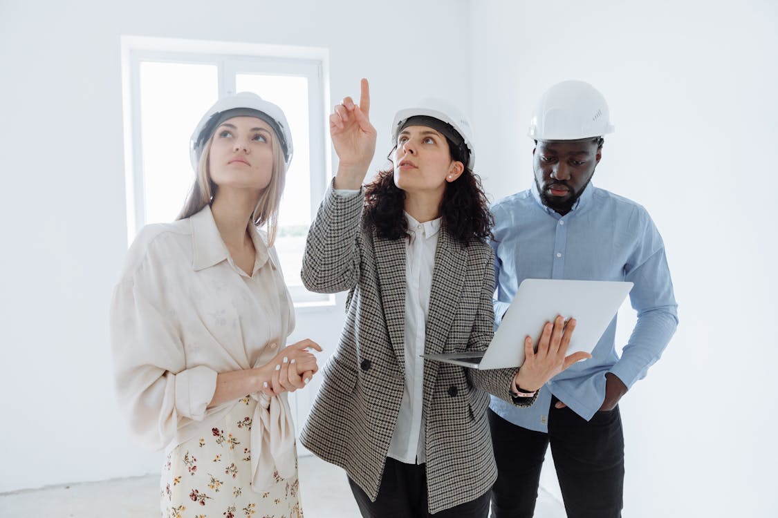 Free A diverse team of architects wearing helmets discusses interior plans with a laptop in a bright room. Stock Photo