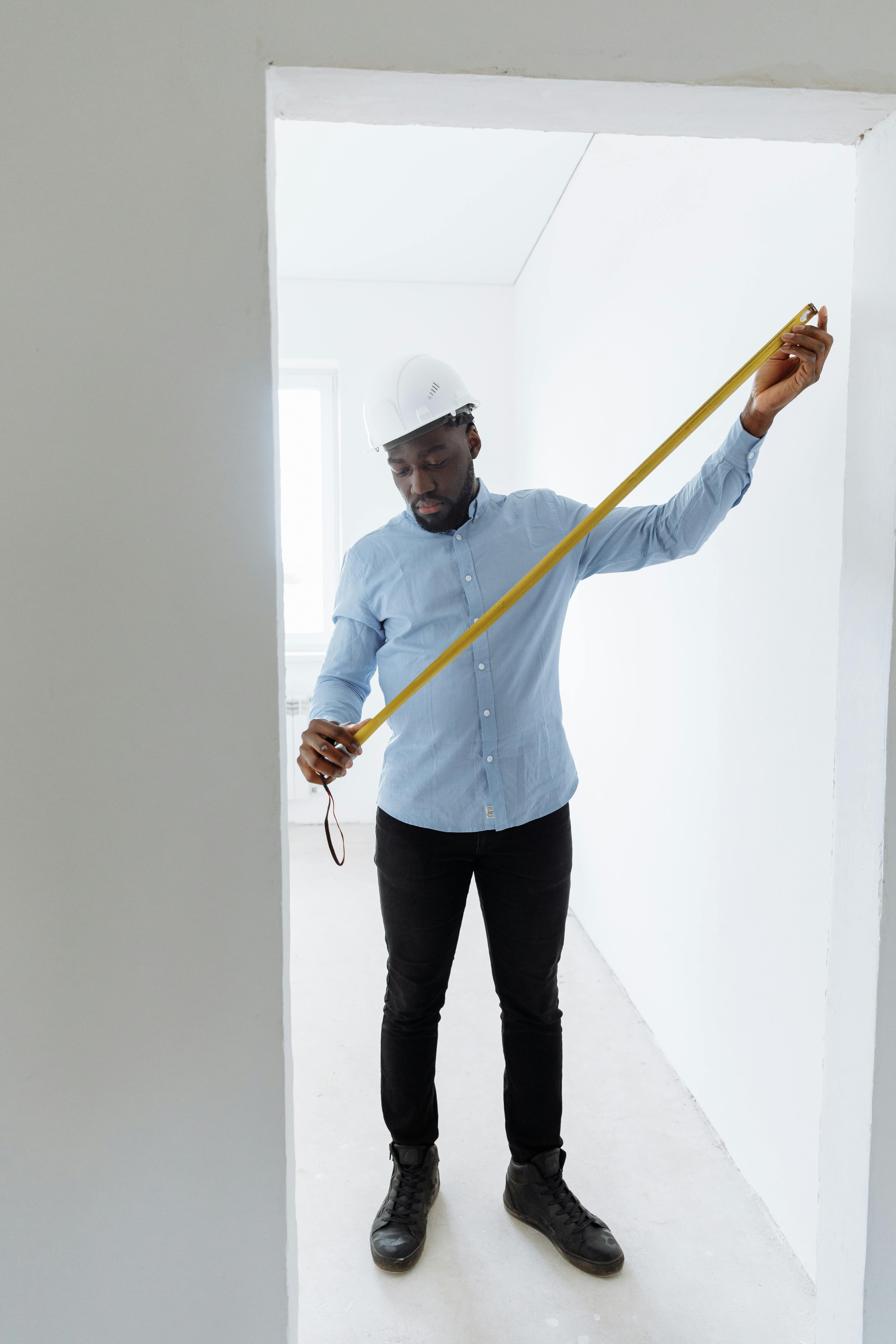 Adult male construction worker measuring room dimensions with a tape measure.
