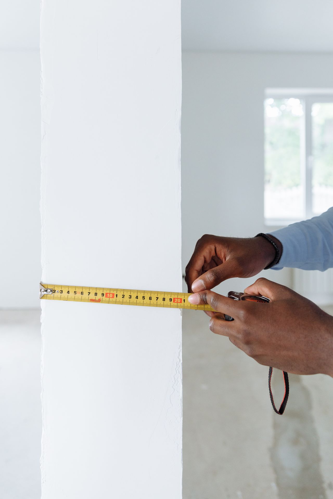 Person measuring a wall with a yellow tape measure before buying furniture