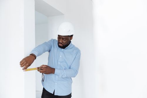 Free A man in a hard hat measures a wall, showcasing precision in a building interior. Stock Photo