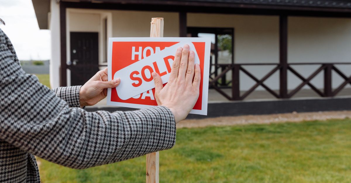 Close-up of hands placing sold sticker on sign in front of a new house.