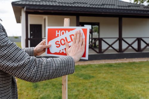 Free Close-up of hands placing 'sold' sticker on sign in front of a new house. Stock Photo