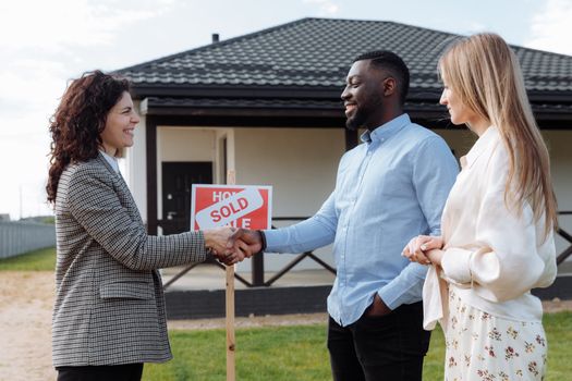 Real estate agent sealing a deal with a diverse couple in front of their new house.