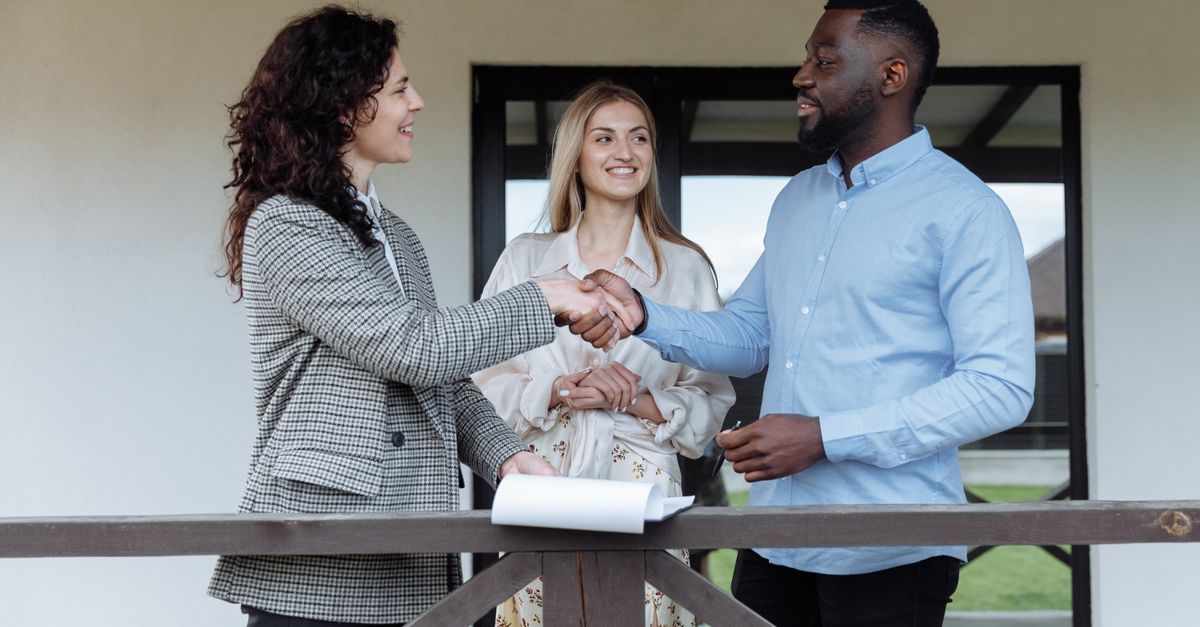 Three adults sealing a real estate deal with a handshake on a porch.