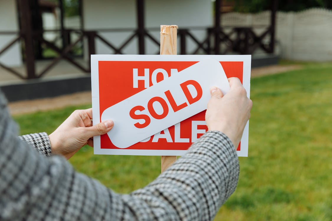 A Faceless Individual Putting a “Sold” Sign Over a “House for Sale” Sign