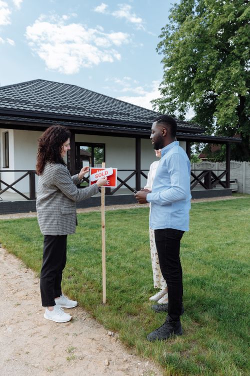 Free A couple celebrates buying a new home, placing a sold sign in the yard on a sunny day. Stock Photo
