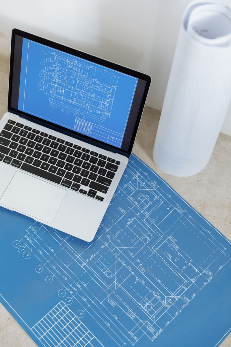 Laptop showing an engineering drawing beside rolled plans