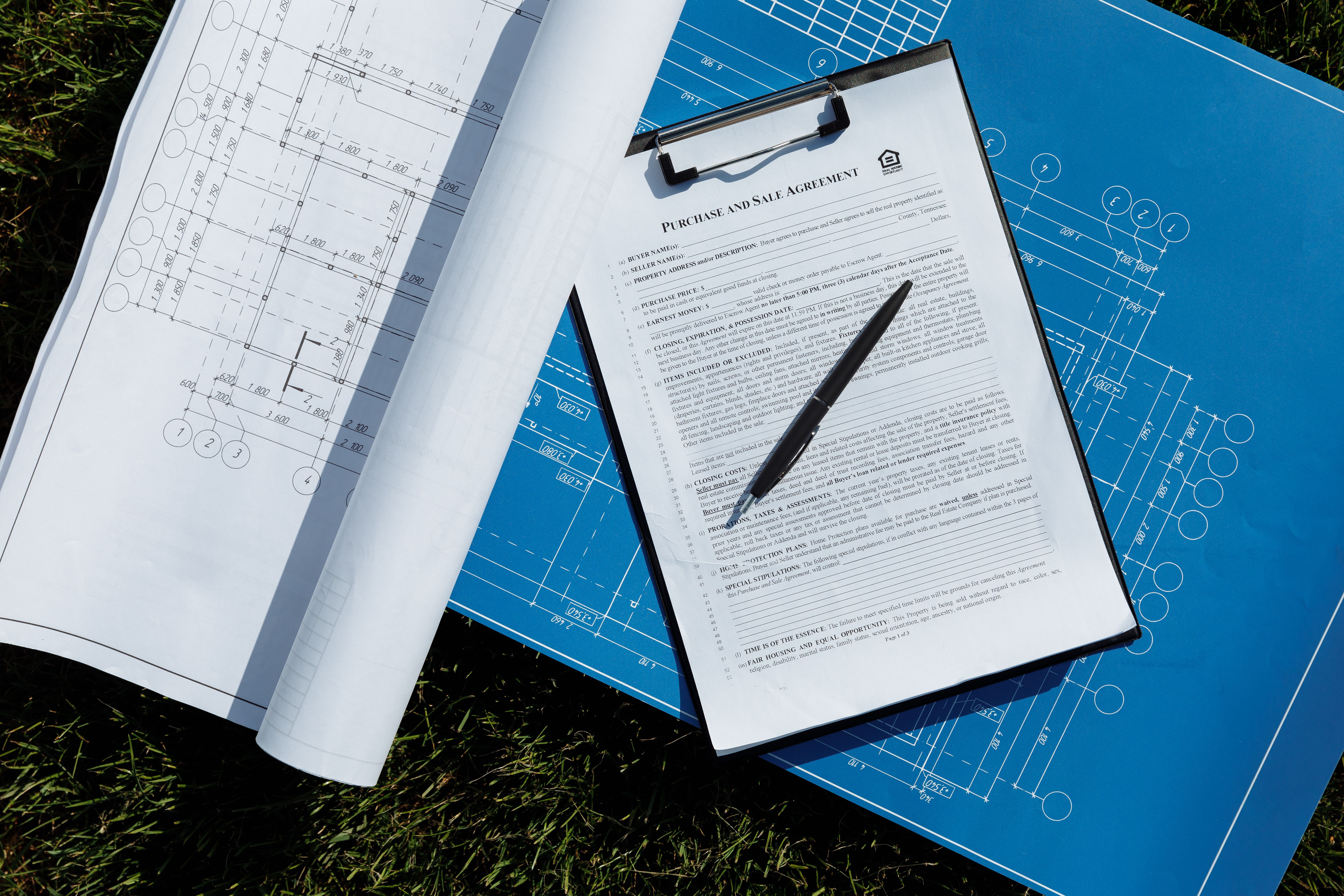 Overhead view of architectural b lueprints and a contract with pen on grass
