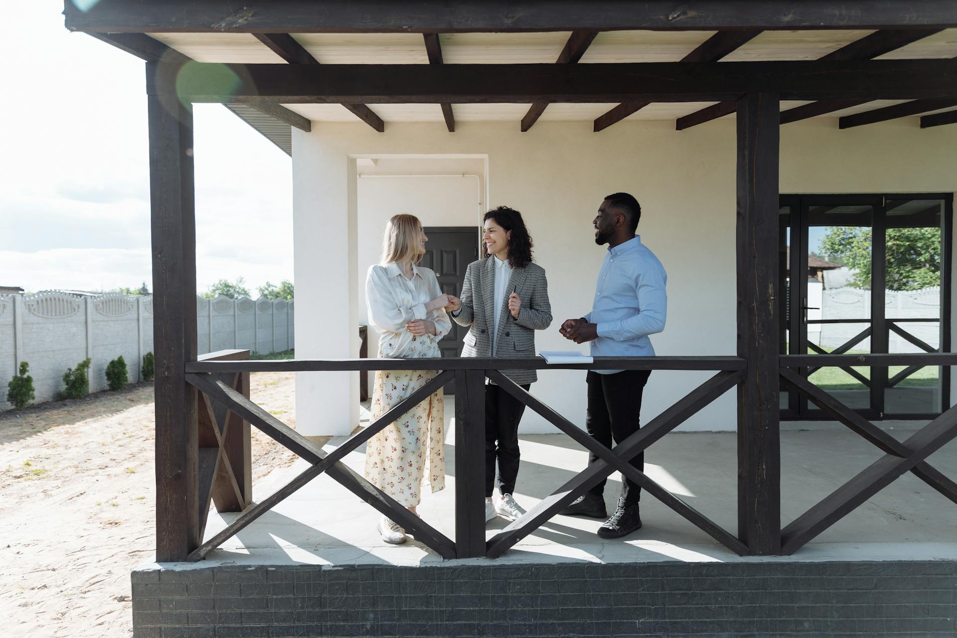 A real estate agent discussing property details with clients on a sunny porch.