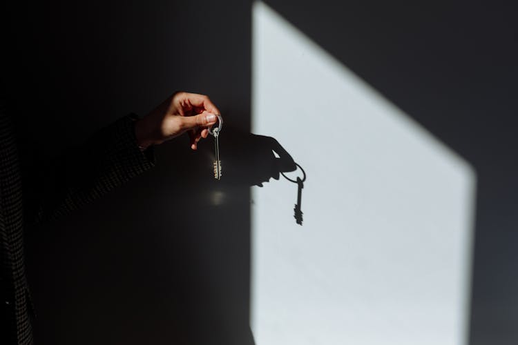 Shadow Of A Hand Holding A Key On Wall