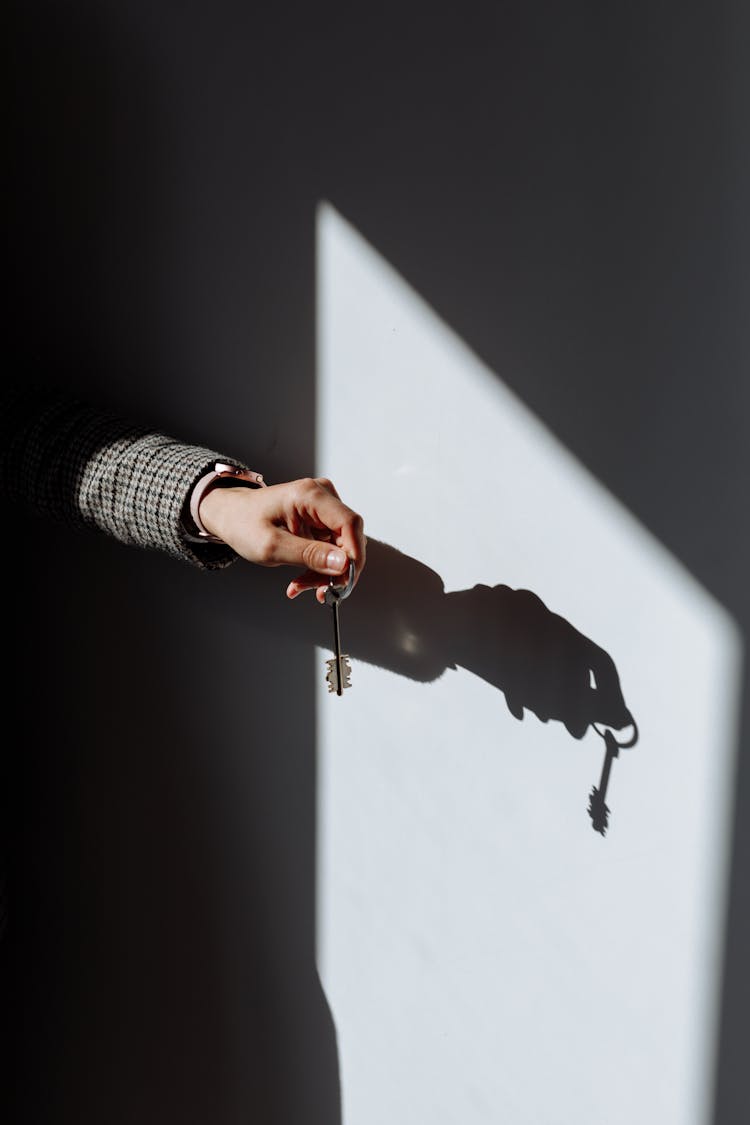 Shadow Of A Hand Holding A Key On Wall