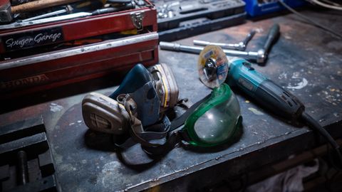 Close-up of a workshop with safety gear, grinder, and toolbox on a metal surface.