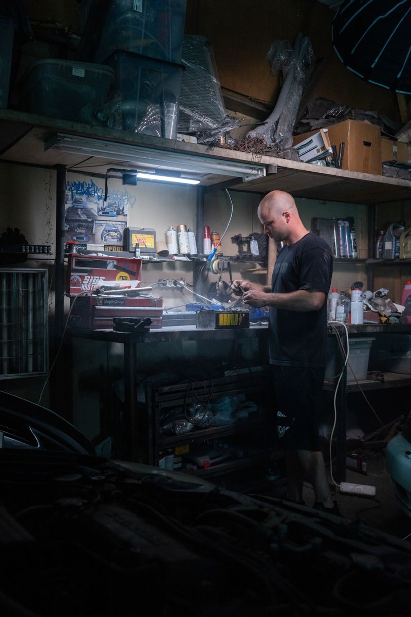 A mechanic diligently works on repairs in a dimly lit garage workshop, surrounded by tools.