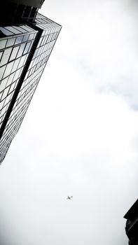 A minimalist shot of a modern skyscraper against the sky with a distant airplane visible, creating a powerful vertical composition.