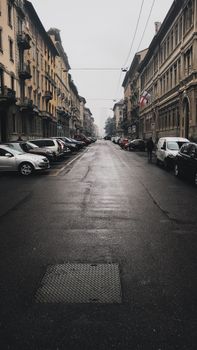 A quiet, rainy street in Milan, showcasing historic architecture and parked cars.