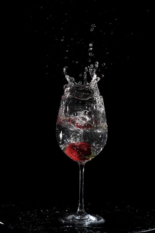 Free A dramatic splash of strawberries in a wine glass against a black background, showcasing movement and elegance. Stock Photo