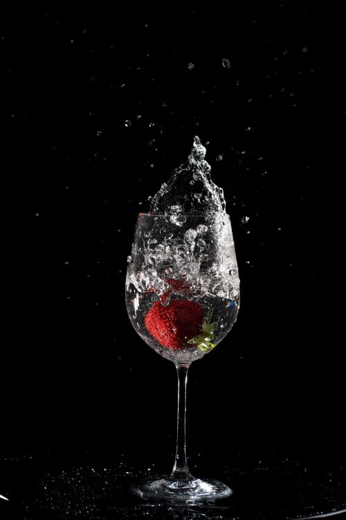 Free A vibrant shot of a strawberry splashing into water in a wine glass, creating dramatic water droplets. Stock Photo