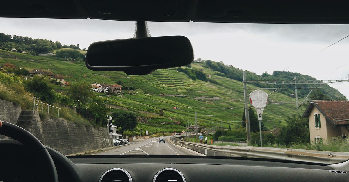 Blick aus dem Auto auf eine kurvige Landstraße durch grüne Hügellandschaft