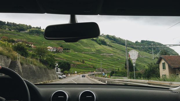 View from a car interior driving through a picturesque rural hillside with lush greenery.