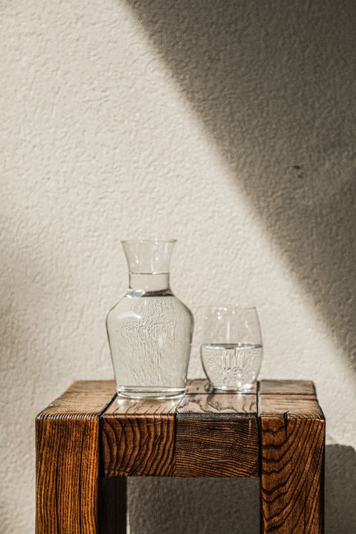 Free Glass pitcher and tumbler on wooden table, sunlight casting shadows. Stock Photo