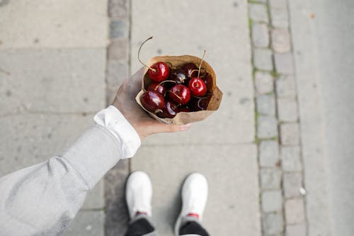 Person Holding a Brown Paper Bag with Cherries