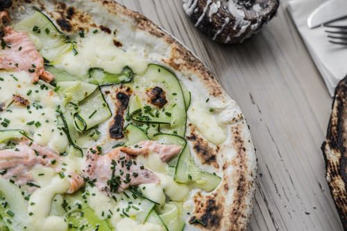 Free Artisan pizza topped with salmon, cucumbers, and cheese, featured on a wooden board. Stock Photo